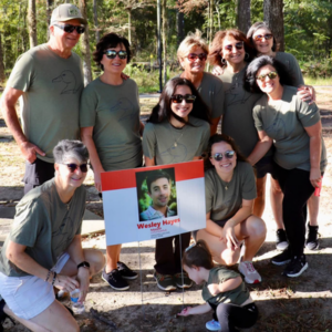 Olivia Hayes and family in matching green duck-design shirts gather around a MADD Louisiana sign with Wesley Hayes’s photo as a little girl plays at its base.